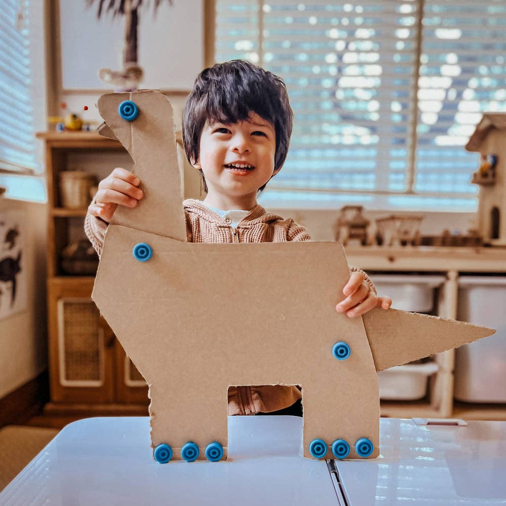 Smiling boy holds a large cardboard dinosaur assembled with bright blue plastic screws.
