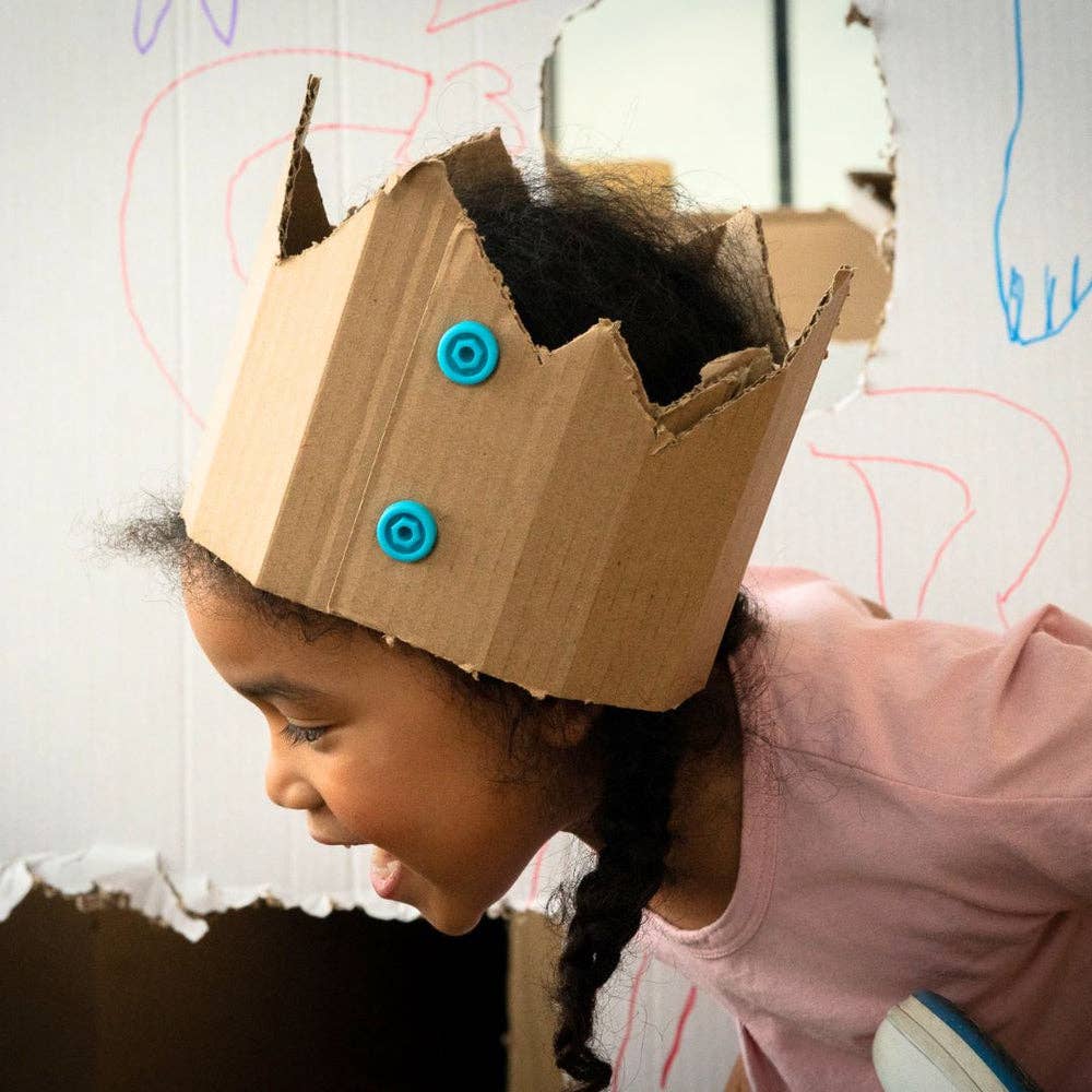 Young girl wearing a jagged cardboard crown fastened with two bright blue plastic Makedo connector pieces.