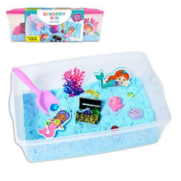 Mermaid sensory bin with blue sand, pink scoop, mermaid figures, and a treasure chest inside a clear plastic tub.