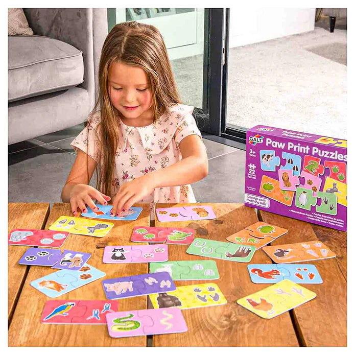Girl matching colorful animal and footprint puzzle pieces on a wooden table next to a purple toy box.