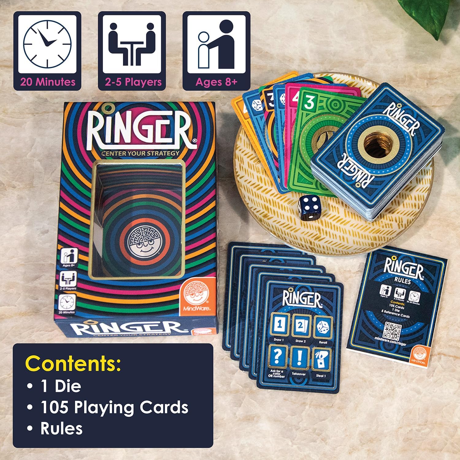 Ringer card game box with colorful rings, a stack of hole-punched cards, a blue die, and rules for 2-5 players.
