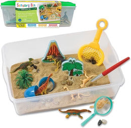 A clear sensory bin filled with sand, toy dinosaurs, a volcano, a tree, a yellow sifter, and a red paintbrush.