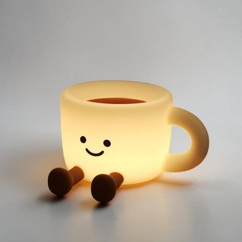 Glowing yellow cup-shaped silicone lamp with a black smiley face and two brown feet on a white surface.