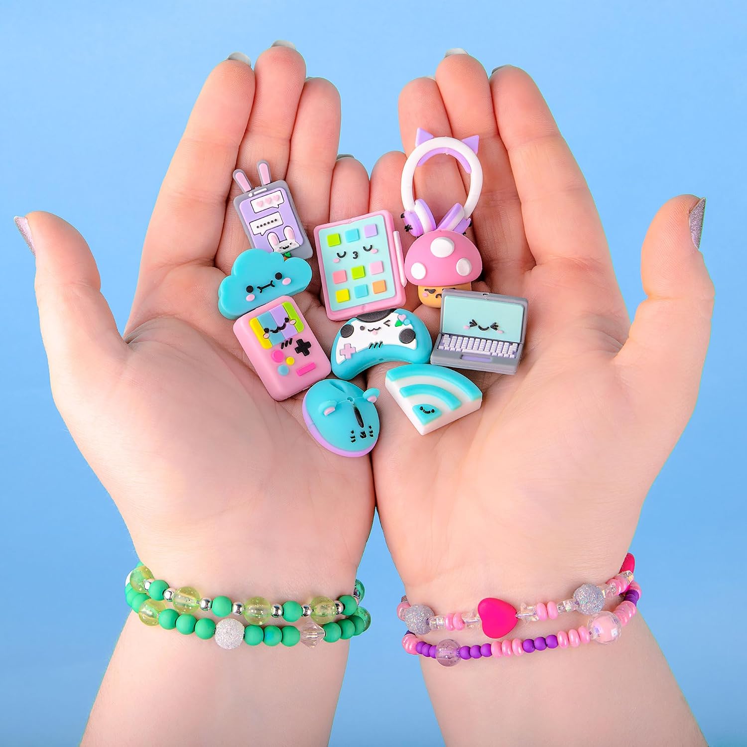 Hands holding various pastel-colored charms shaped like a laptop, game controller, and cloud with cute faces.