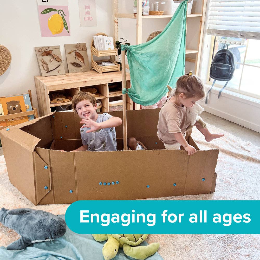 Two children playing in a large cardboard boat built with blue Makedo connectors and a green fabric sail.