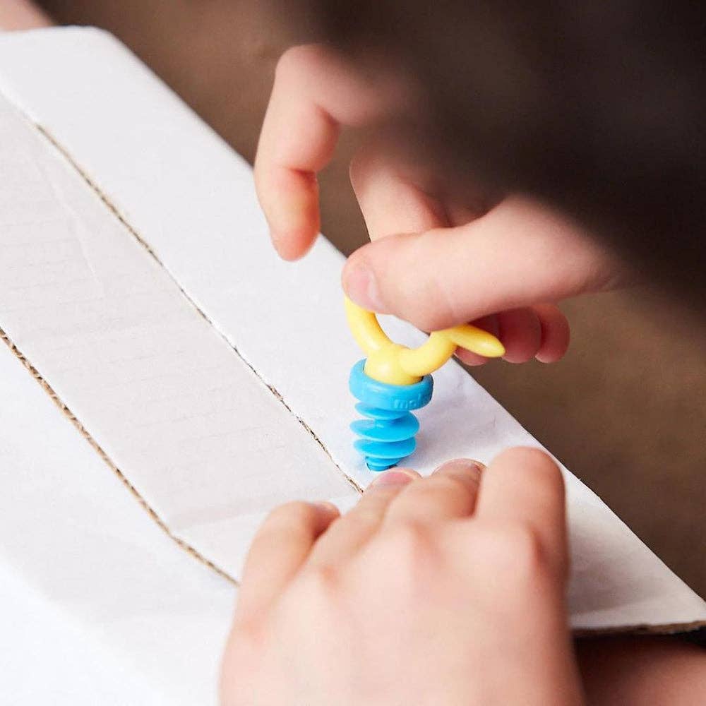 Child's hands twisting a blue and yellow plastic screw tool into a piece of white cardboard.