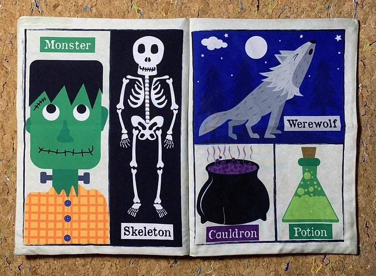 An open fabric book or pouch laid flat on a cork background, showing two illustrated panels: the left panel features a green monster and a white skeleton labeled 'Monster' and 'Skeleton'; the right panel shows a gray werewolf under a moon, a black cauldron, and a green potion bottle labeled 'Werewolf', 'Cauldron', and 'Potion'.