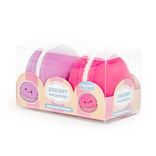 A clear plastic box containing two soft, round squishy macarons in purple and pink colours.