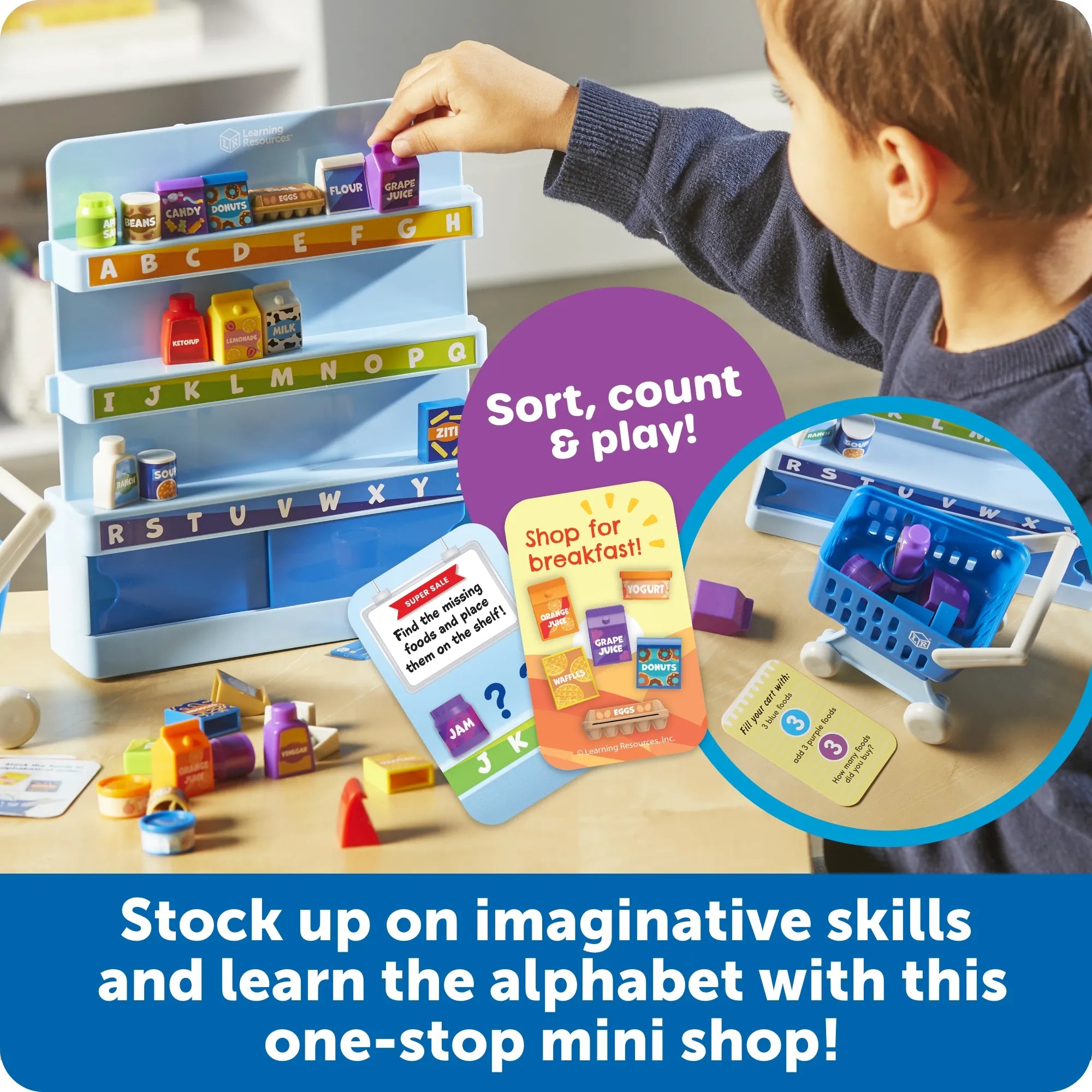 A child is playing with a toy alphabet mini shop set on a tabletop. The set includes a light blue shelving unit with alphabet labels, small toy products, a shopping cart, cards, and loose pieces.