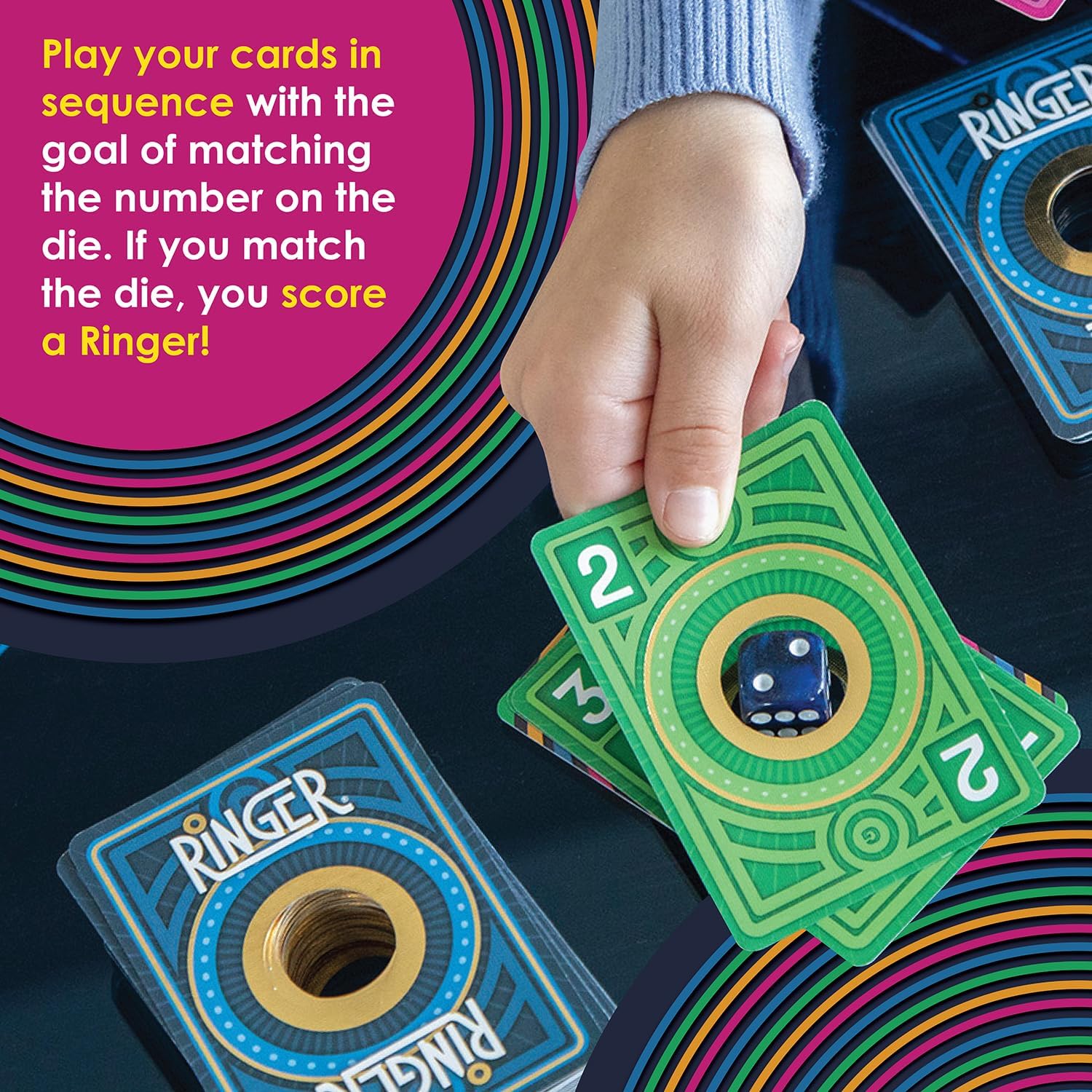 Hand holding a green card with a circular cutout over a blue die, showing a match with the number 2.