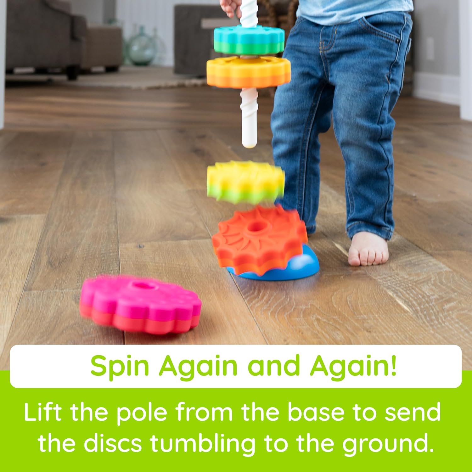 Toddler lifts white spiral pole from a blue base, sending colorful gear discs spinning onto a wooden floor.