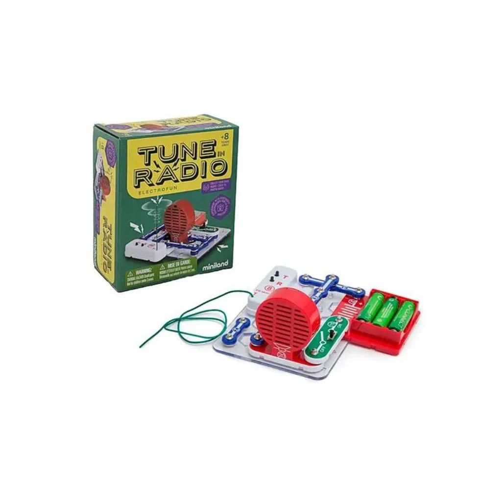 A DIY radio circuit kit with a red speaker and green battery pack assembled on a base next to its green box.